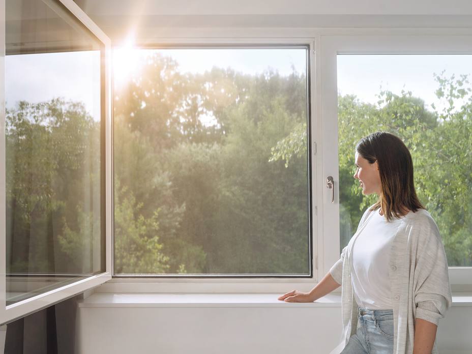 Herstellerbild. Frau an Fenster mit Pollenschutz von Tesa.