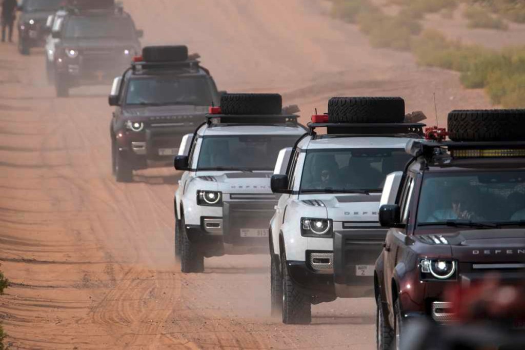 Mehrere Land Rover Modelle fahren eine Sandpiste entlang.