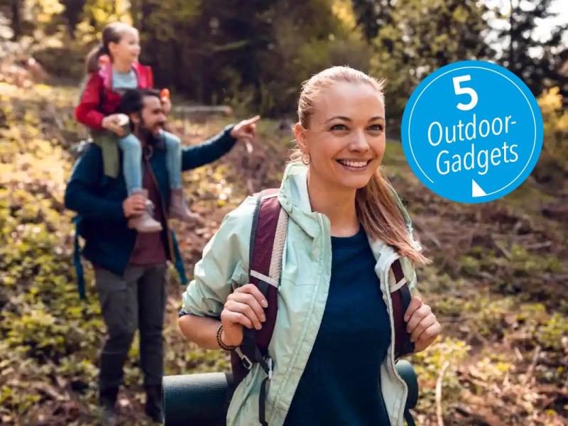 Eine dreiköpfige Familie, die mit Rucksack und Isomatte durch einen Wald wandert.