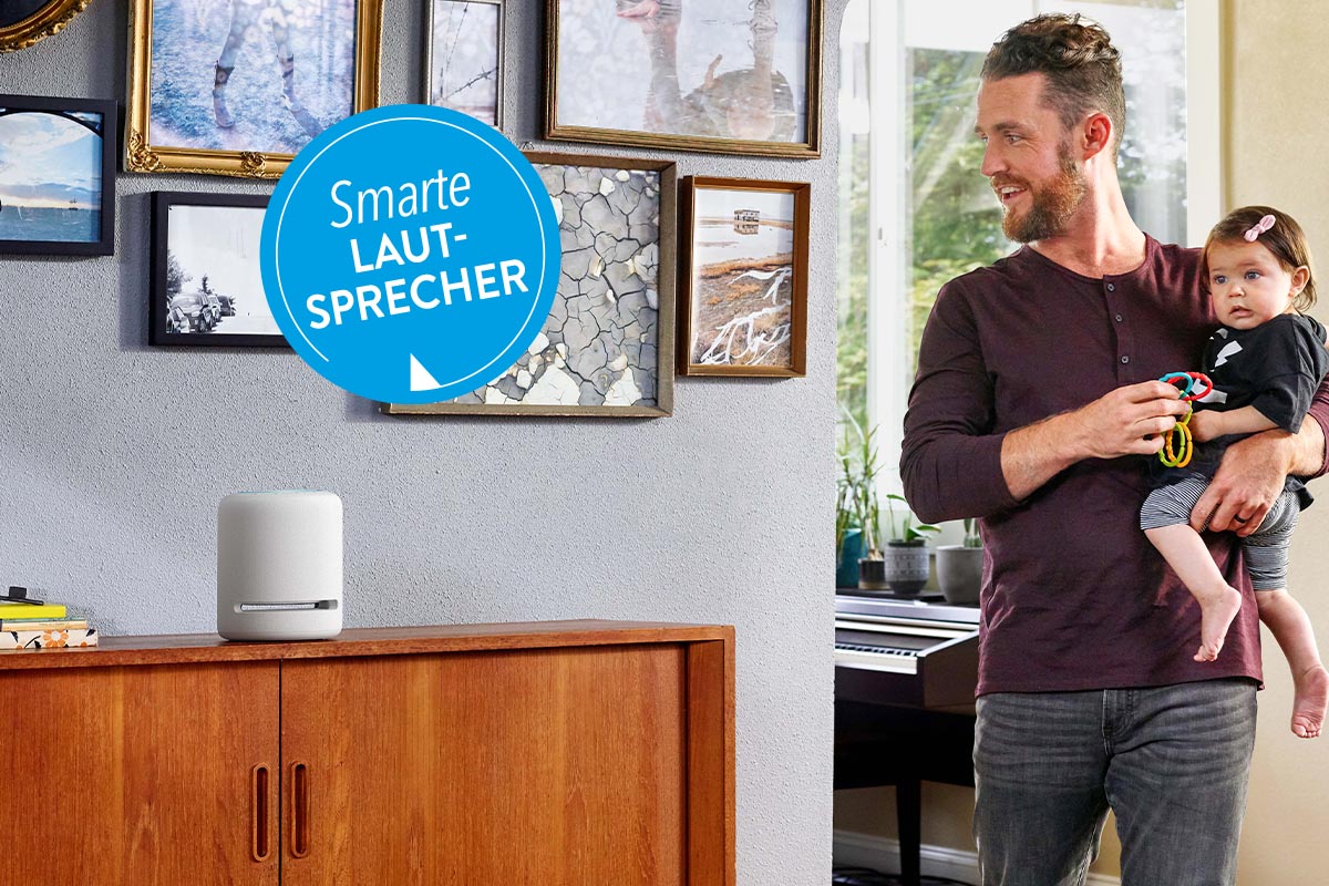 Vater mit Kind auf dem Arm neben einem Smart Speaker stehend.