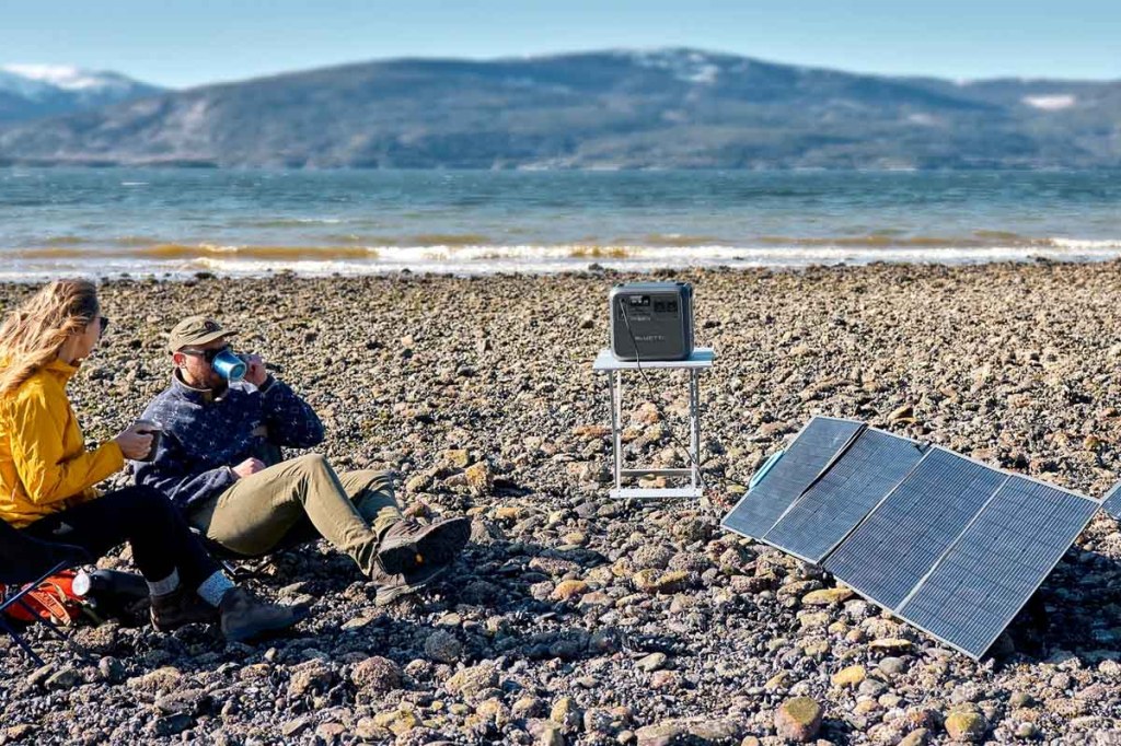 Ein Paar sitzt auf einem Steinstrand mit der neuen Bluetti-Powerstation und Solarpanels.