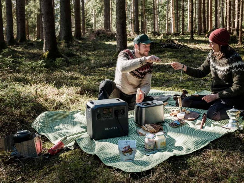 Ein Paar mit Bluetti-Powerstation auf einer Picknick-Decke im Wald.