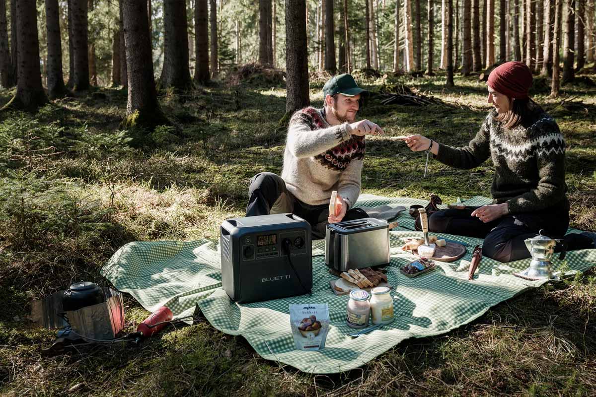 Ein Paar mit Bluetti-Powerstation auf einer Picknick-Decke im Wald.