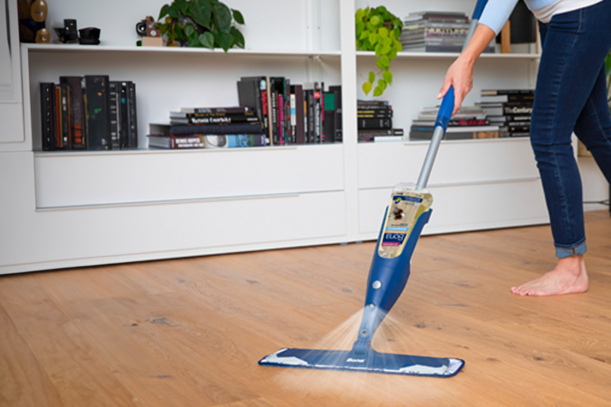Eine Person putzt einen Holzfußboden in einem Wohnzimmer mit dem Bona Spray-Mop.