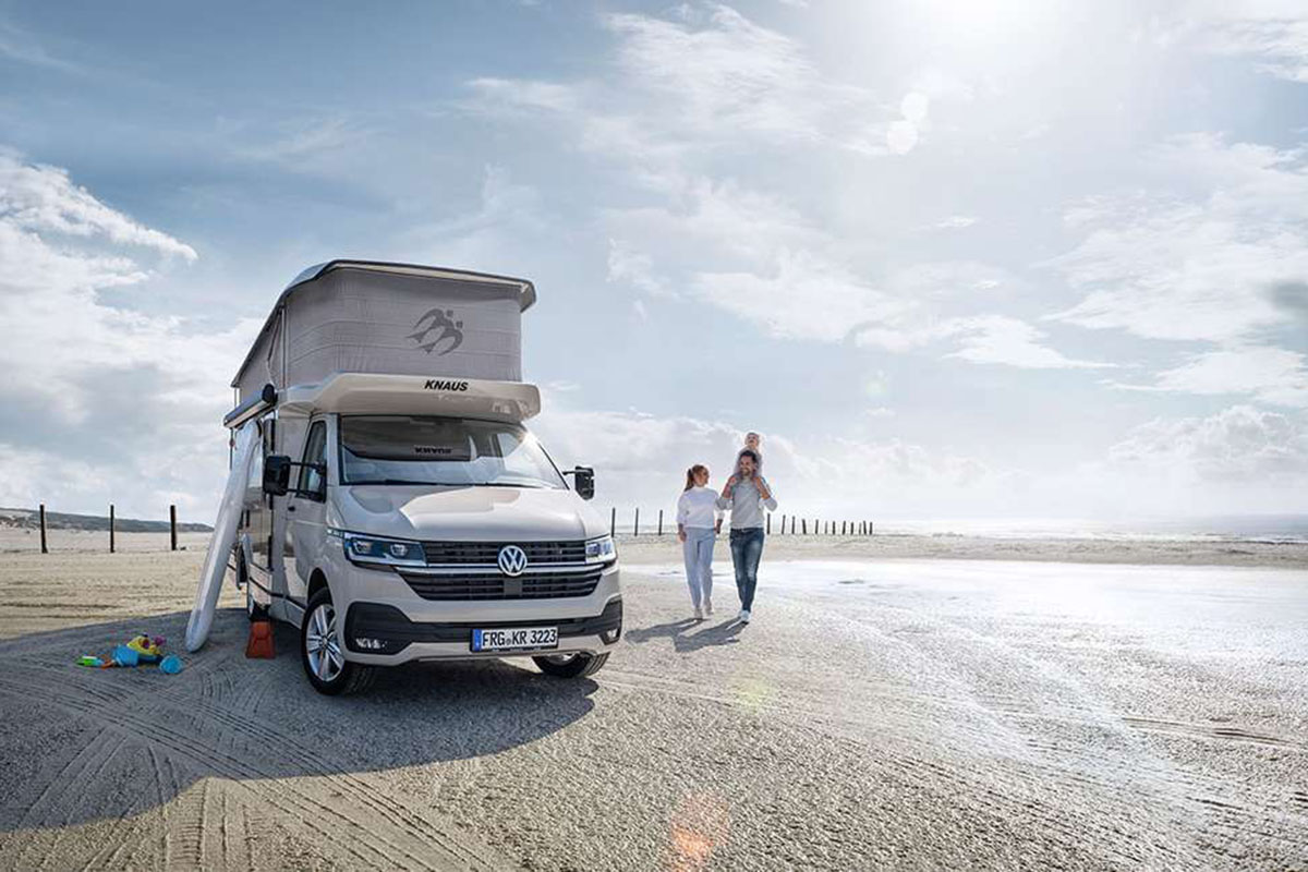 Camper Van-Alternative zum VW California: Ein Weinsberg X-Cursion steht mit aufgestelltem Hubdach auf einem Strand-Parkplatz am Meer.