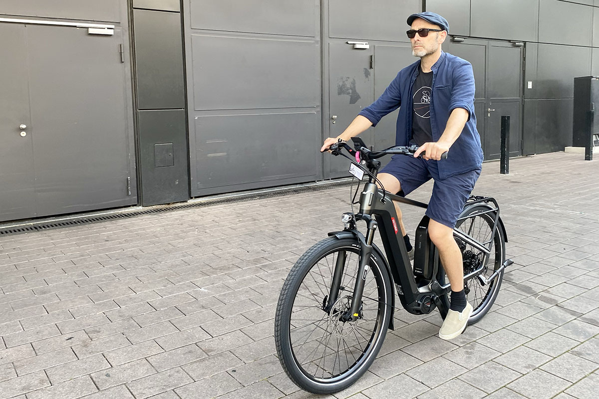 Mann fährt auf E-Bike Victoria Utilyon vor Messestand auf der Eurobike 2023.