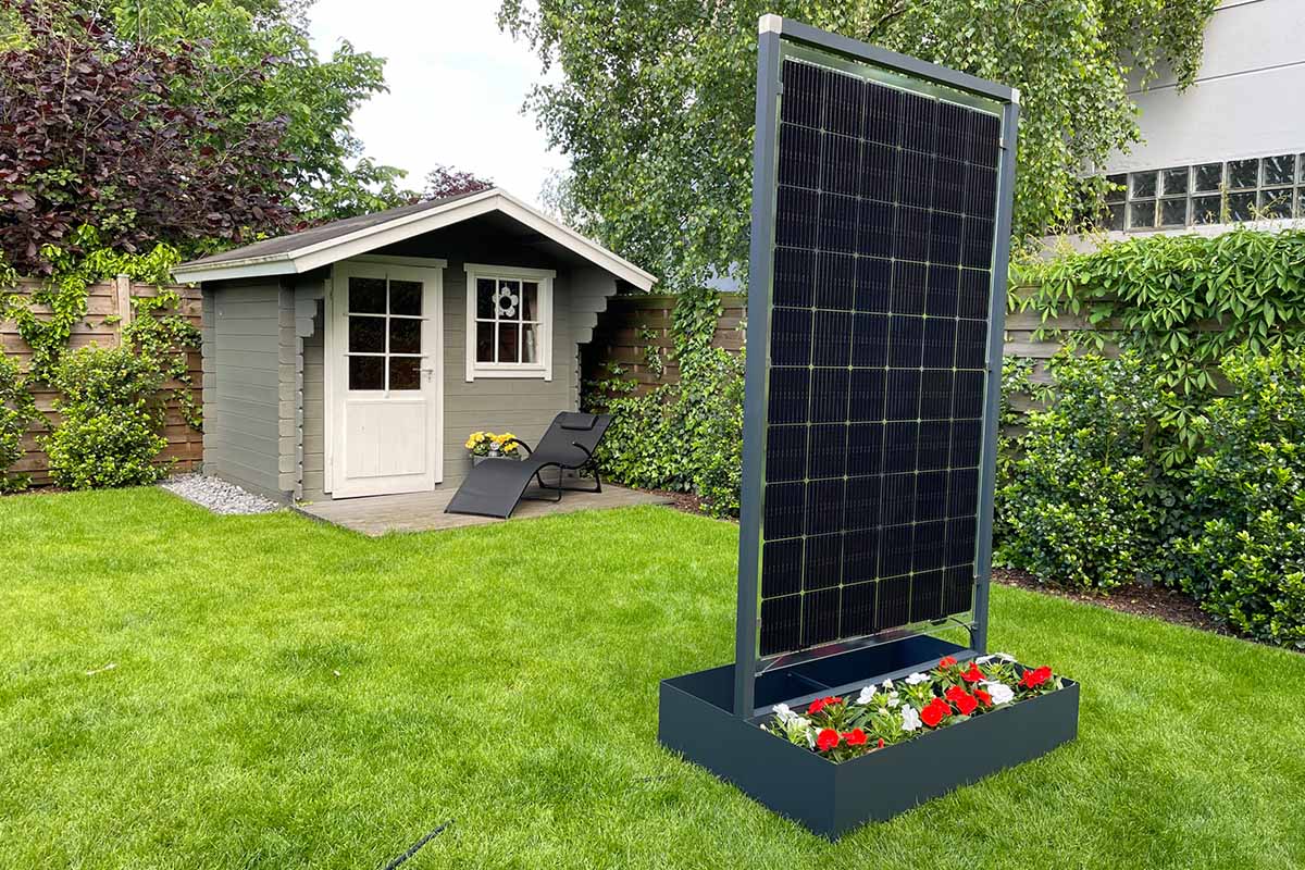 Der neue Solar-Blumenkübel von GreenAkku in einem Garten mit Gartenhäuschen im Hintergrund.