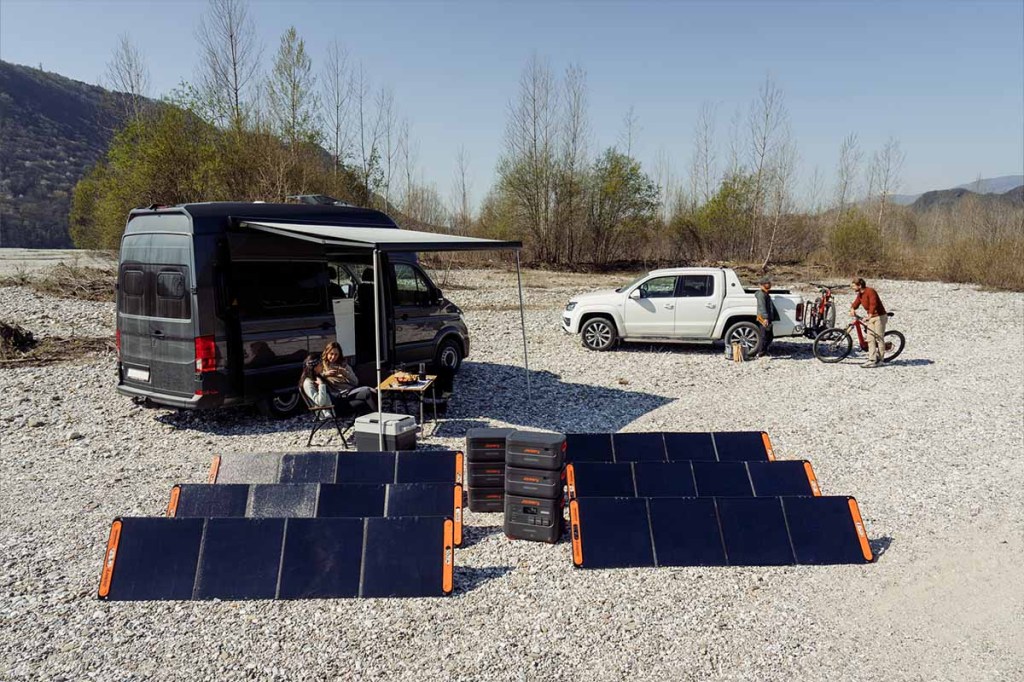 Die neue Jackery-Powerstation mit sechs Solarpanles vor einer Camping-Szene.