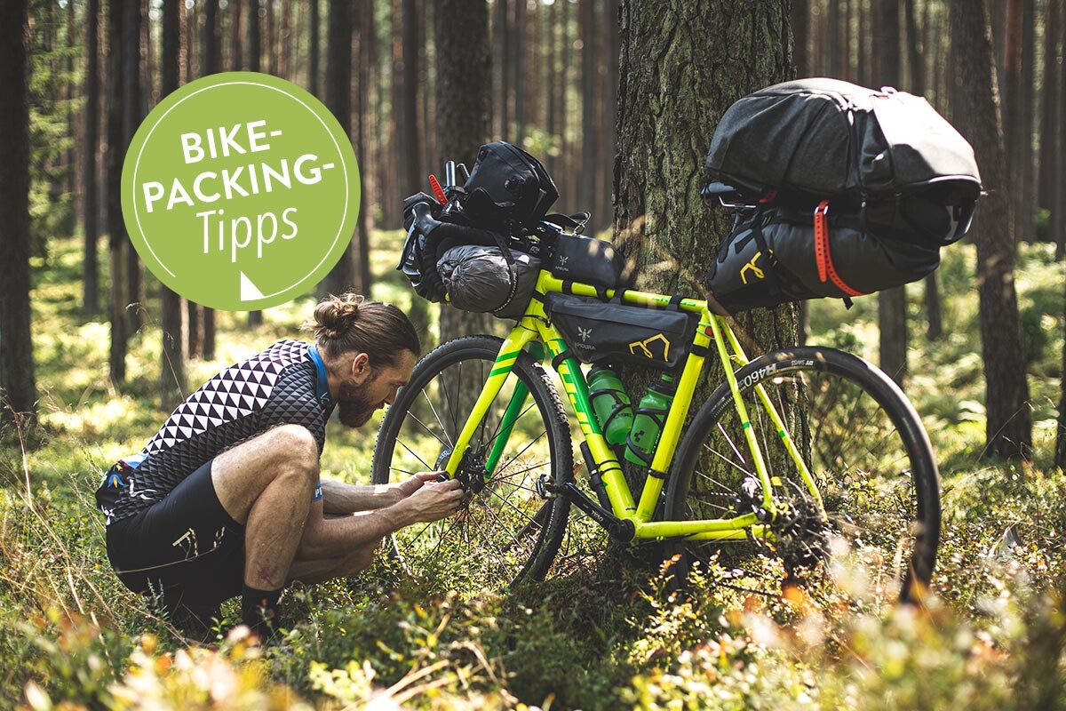 Fahrradfahrer hockt neben seinem Rad im Wald, das Rad ist vollbepackt mit Taschen