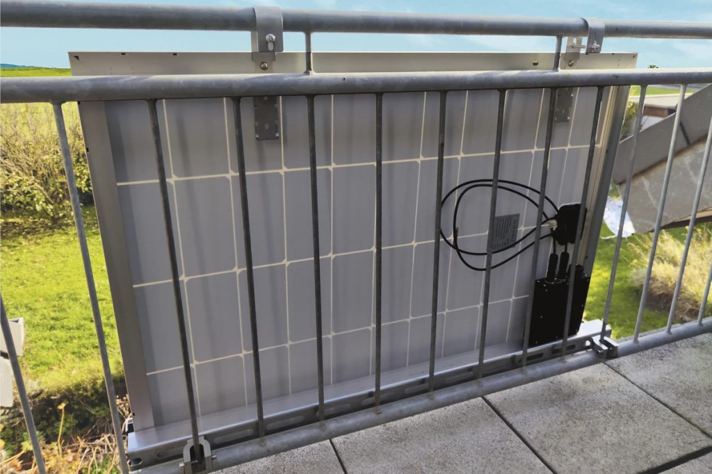 Solarpanel von hinten an Balkongeländer angebracht vor grüner Kulisse