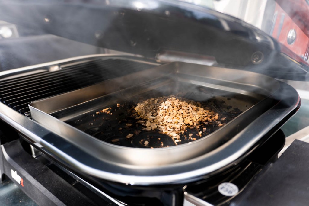 Der Weber Lumin mit halb offenem Deckel und qualmenden Räucherchips in der Schale