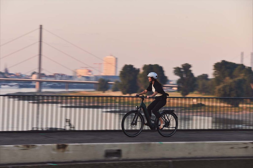 Frau fährt mit E-Bike über ein Brücke bei aufgehender Sonne