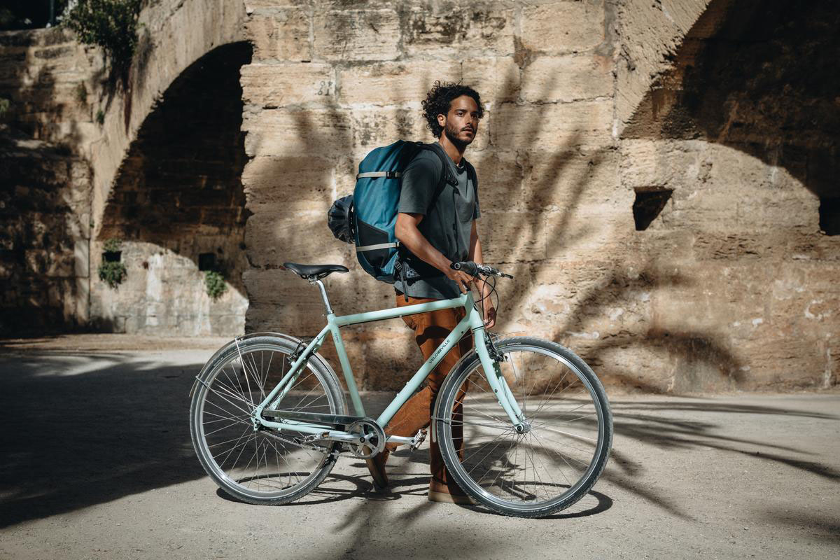 Mann mit E-Bike vor Mauer.