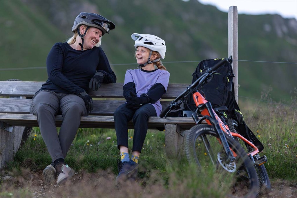 Mutter und Tochter sitzen auf einer Bank, daneben lehnt ein Kinder-E-Bike
