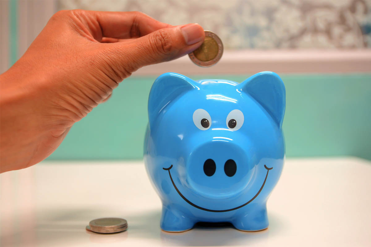 Eine Hand wirft Münzen in ein blaues Sparschwein