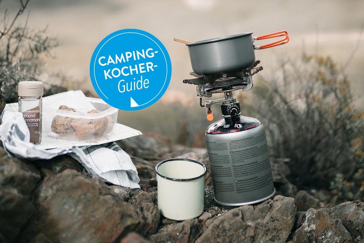 Ein kleiner Campingkocher mit Topf steht auf Felsen.