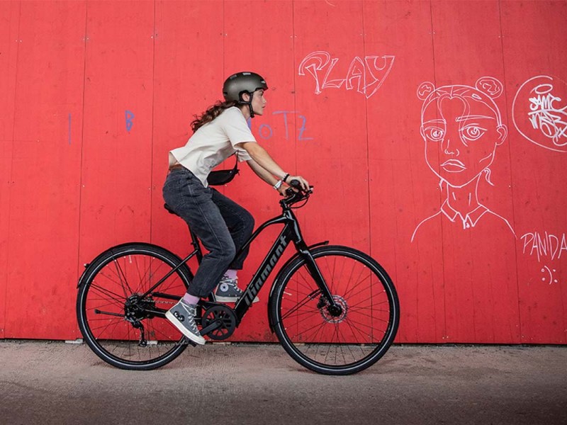 Frau fährt mit einem E-Bike vor einer roten Wand entlang