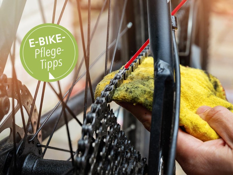 Eine Hand, die ein Tuch hält, putzt die Fahrradkette eines E-Bikes.