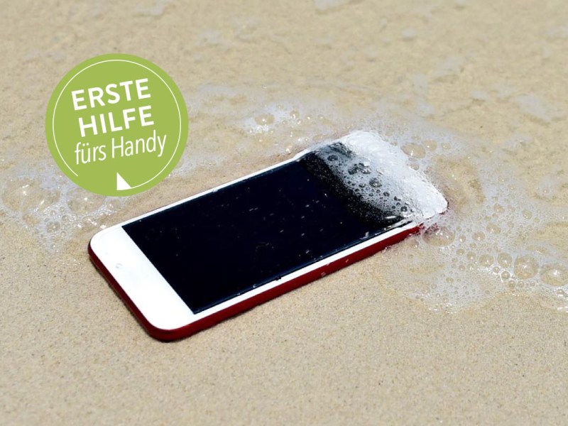 Smartphone liegt am Strand und wird von Meerwasser überspült.