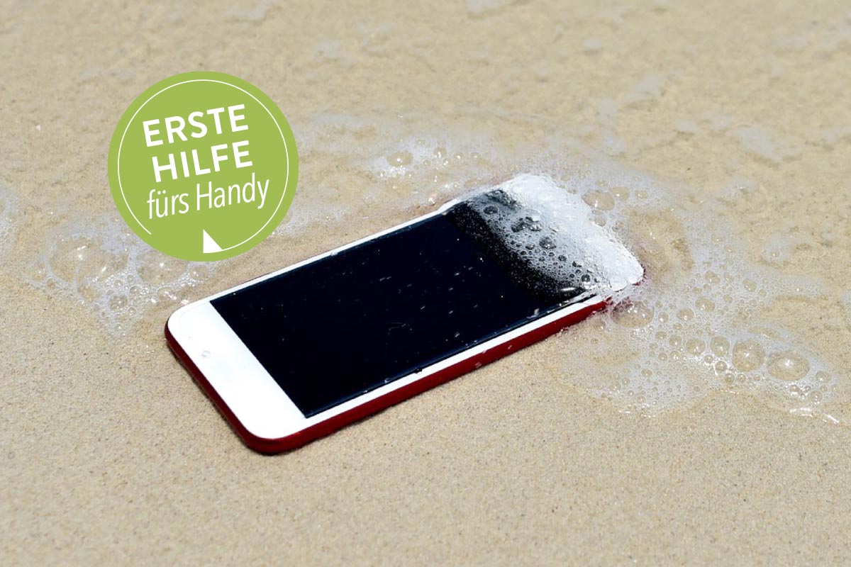 Smartphone liegt am Strand und wird von Meerwasser überspült.