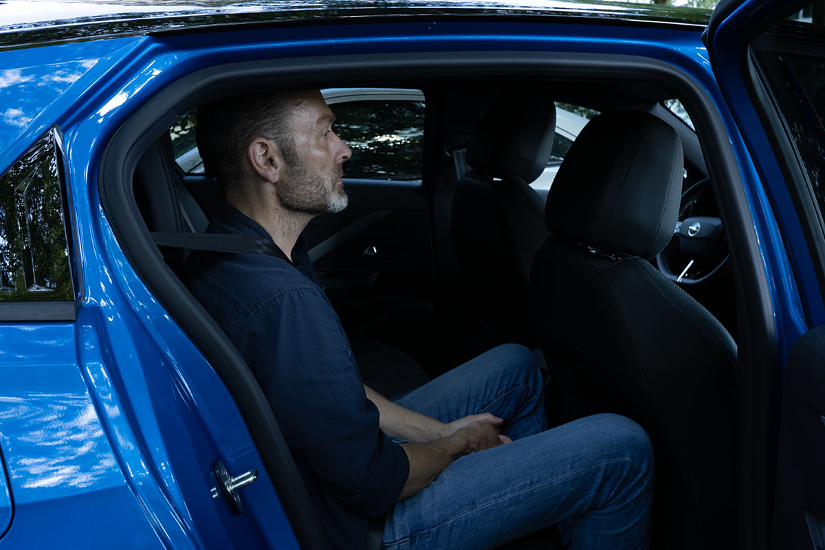 Mann sitzt auf Rücksitz bei geöffneter Tür im E-Auto Opel Astra Electric.