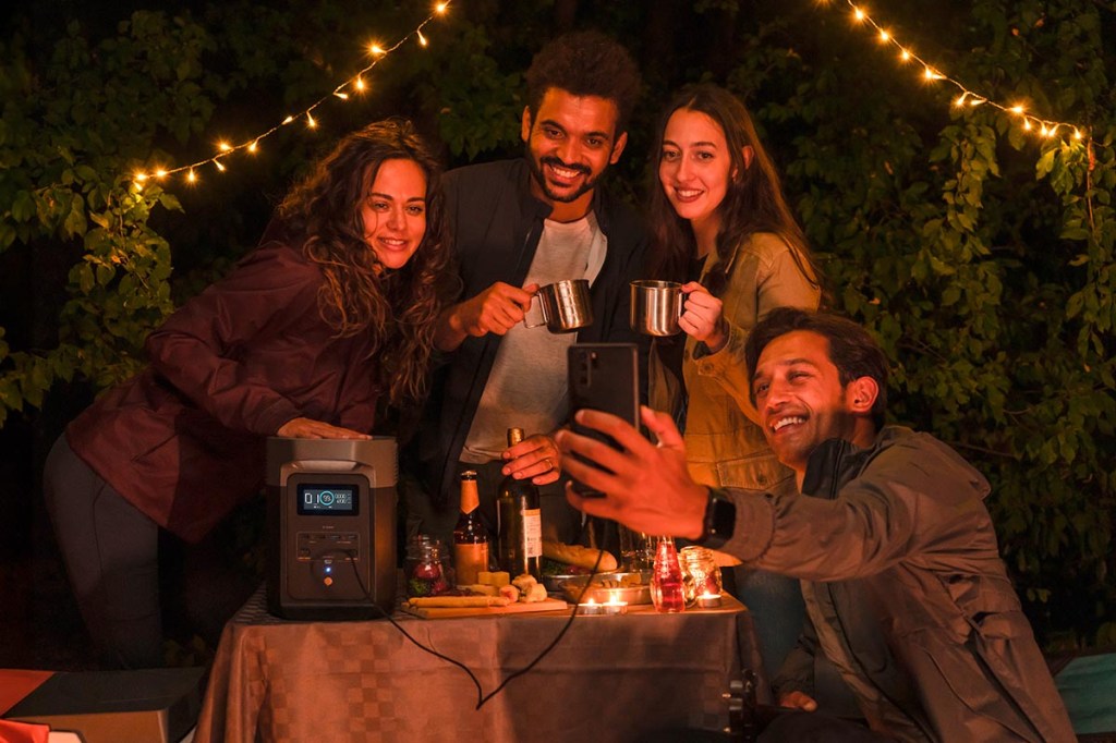 Eine Gruppe von jungen Menschen macht bei stimmungsvoller Gartenbeleuchtung ein Selfie. Auf dem Tisch steht eine Powerstation.