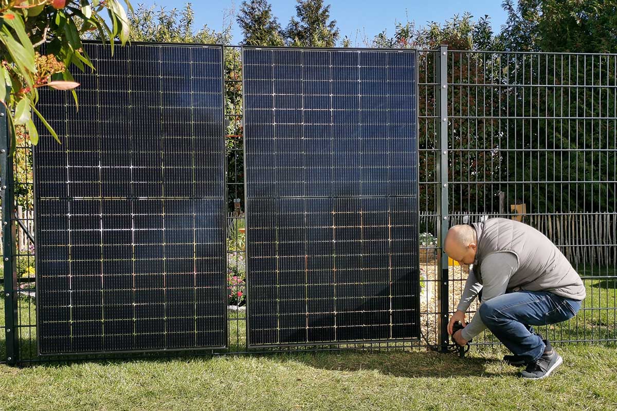 Ein Mann montiert Solarpanels an einem Zaun.
