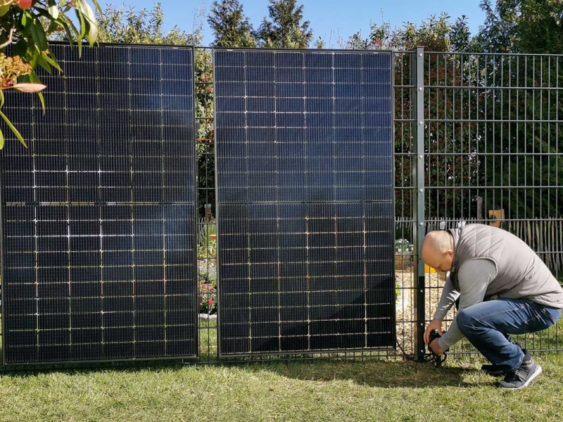 Ein Mann montiert Solarpanels an einem Zaun.