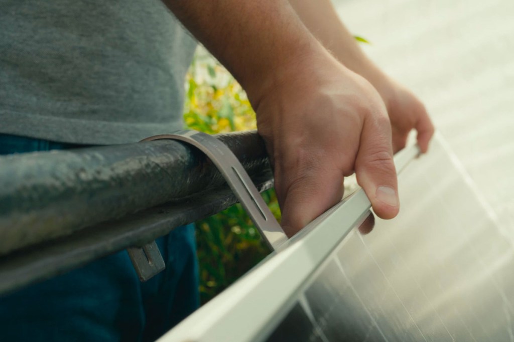 Eine Person montiert ein Solarpanel für ein Balkonkraftwerk an einem Balkongeländer.