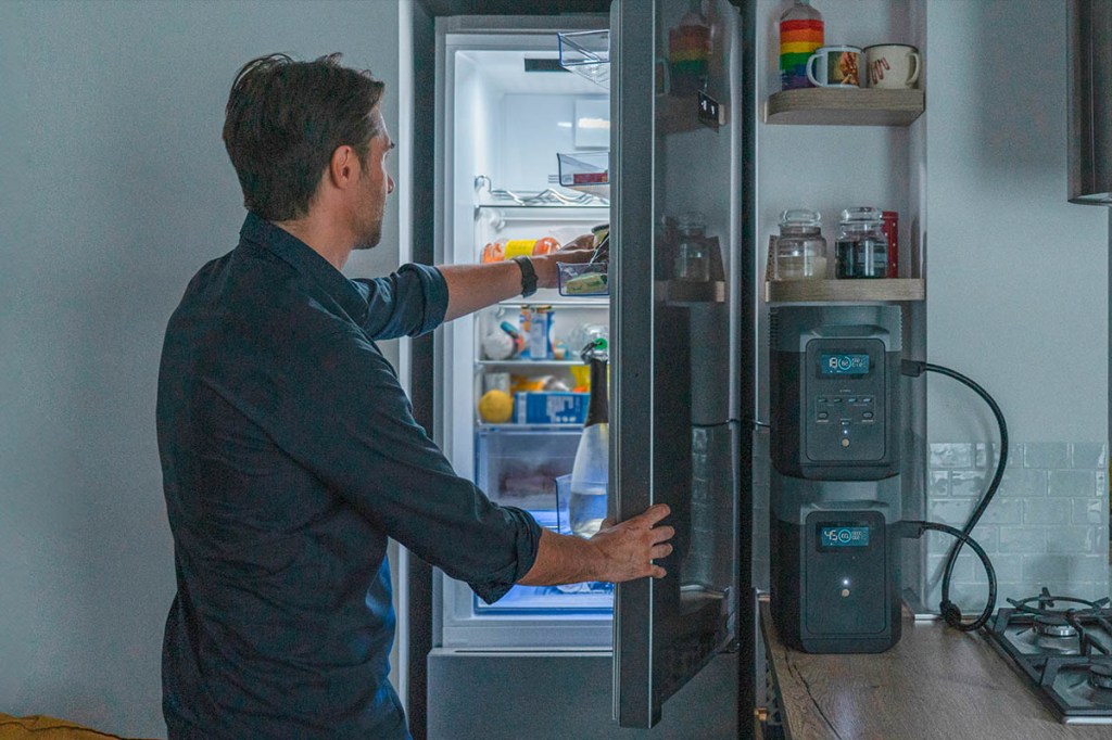Ein Mann holt etwas aus einem großen Kühlschrank. Daneben stehen zwei Powerstations im Regal.