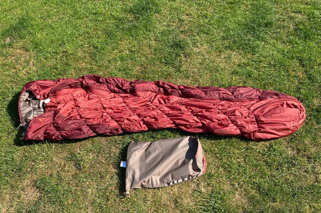 roter Schlafsack auf einer Wiese liegend, daneben ein Sack