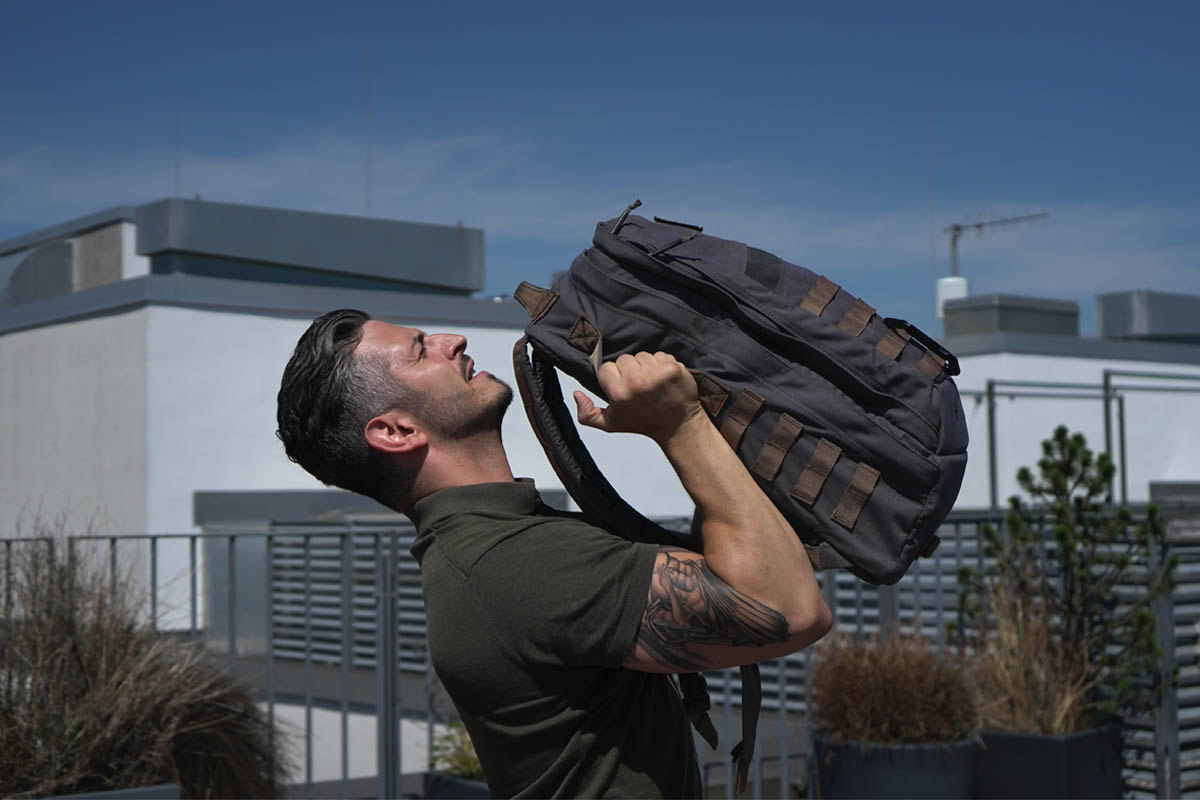 Ein Mann stemmt einen Rucksack in die Höhe.