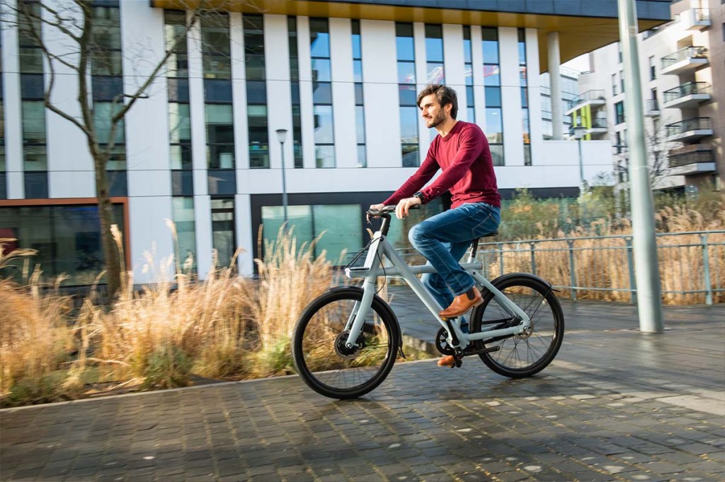 Mann fährt auf einem Fahrrad vor einer Häuserfront her