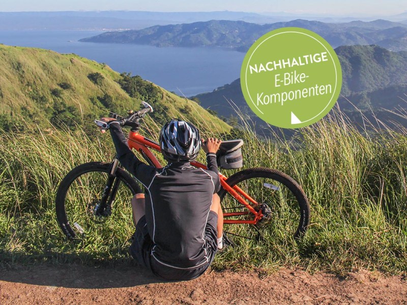 Mann sitzt vor seinem Fahrrad in der Natur, im Hintergrund ist ein See