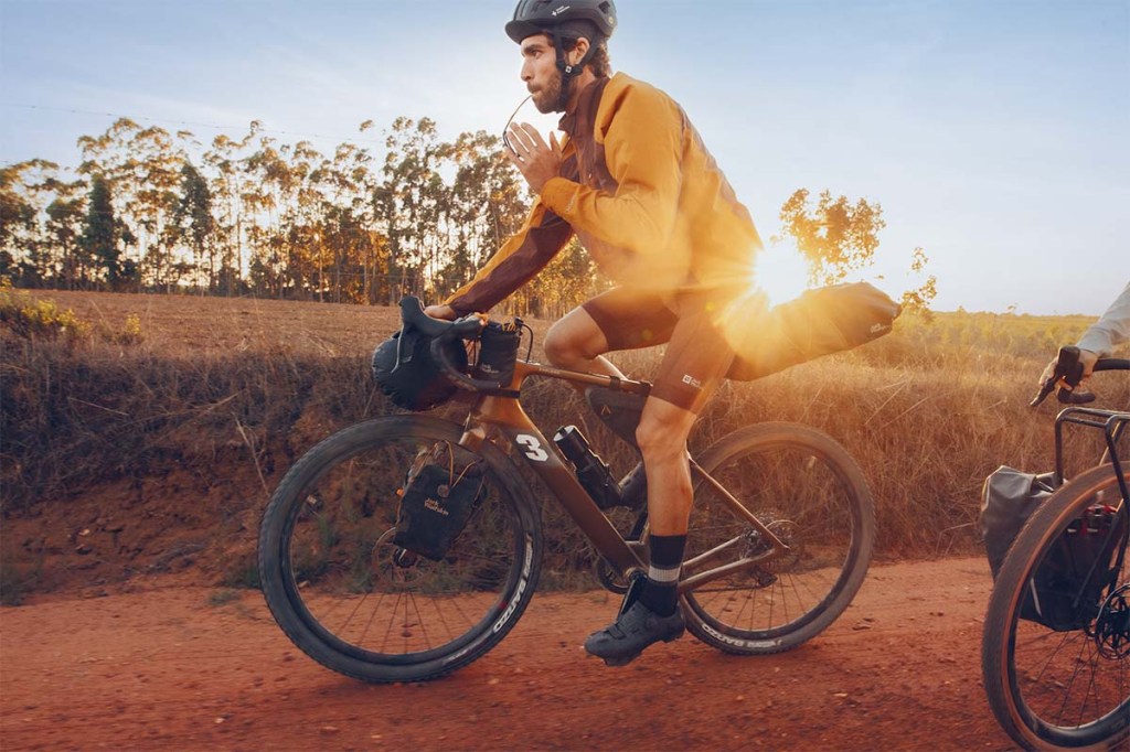 Person fährt mit einem Gravelbike, im Hintergrund die aufgehende Sonne