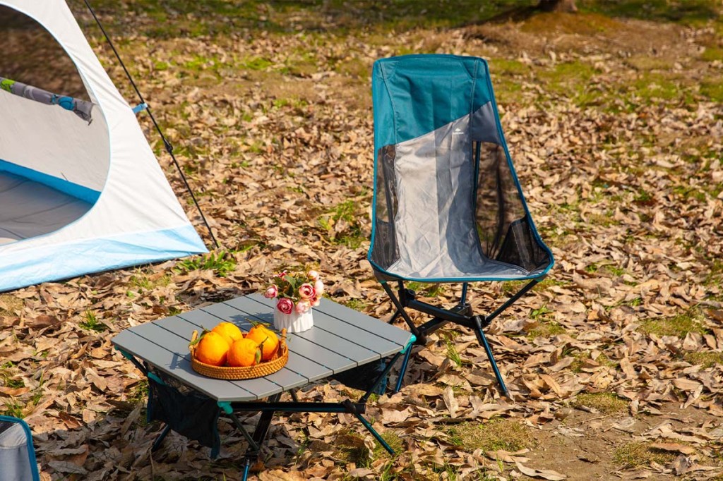 Camping-Tisch und -Stuhl in der Natur, man sieht einen Ausschnitt von einem Zelt im Hintergrund