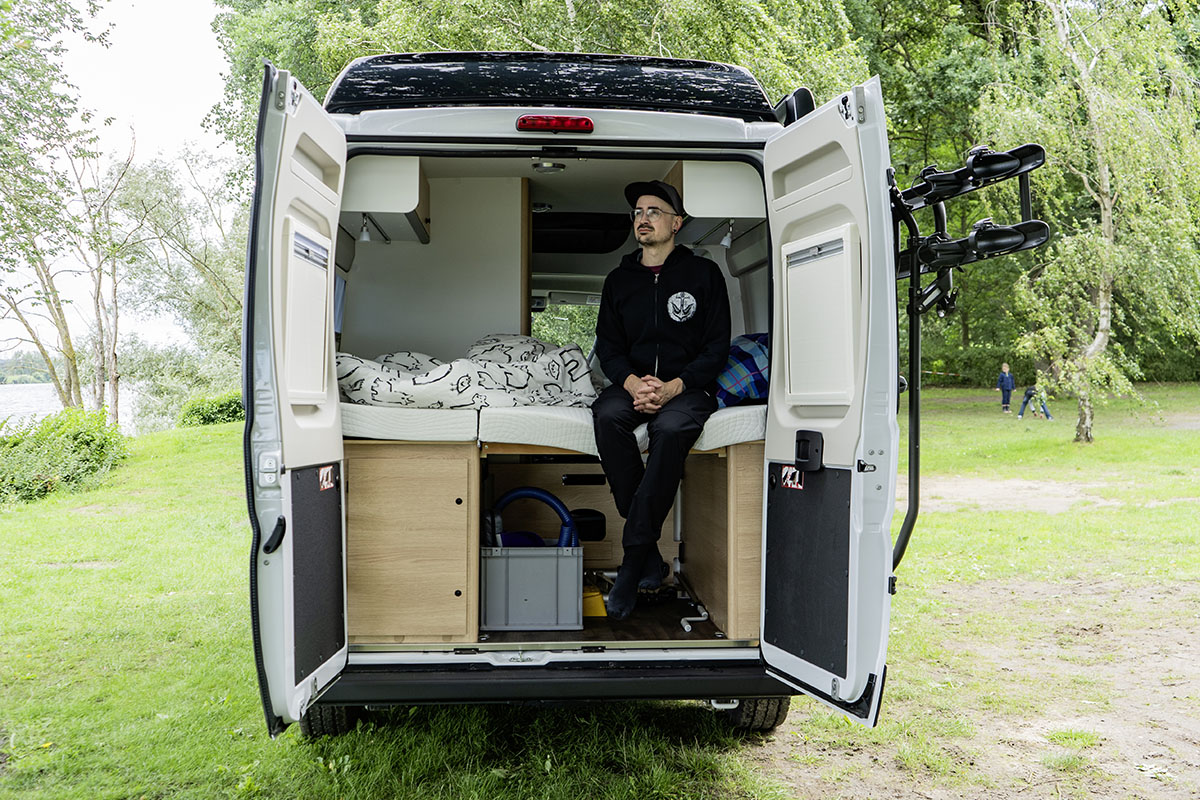 Mann sitzt bei geöffneten Hecktüren auf dem hinteren Bett des Camping-Kastenwagens Sunlight Cliff 540 RT Adventeure Edition.