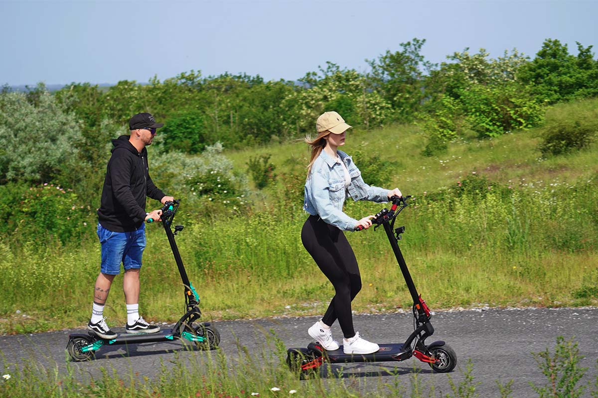 Zwei Personen fahren auf einer Straße im Grünen mit E-Scootern von IO Hawk.