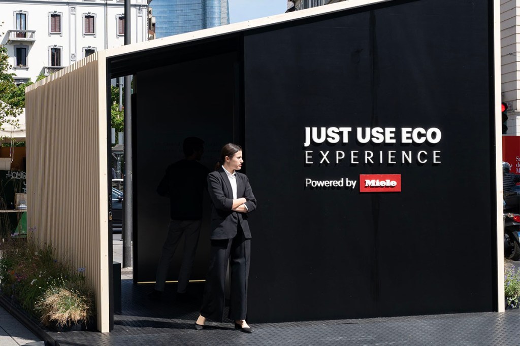 Eine Person verlässt ein kleines Gebäude, auf dem "Just use Eco Experience powered by Miele" steht.