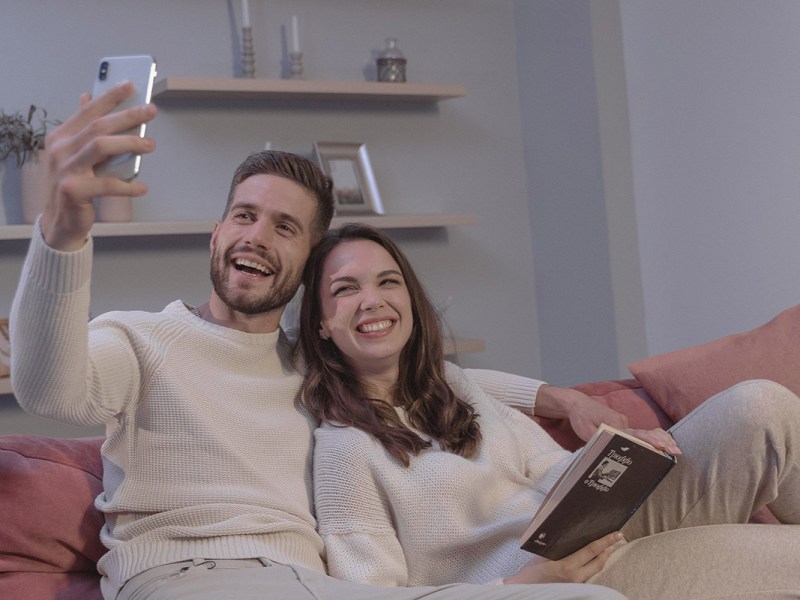 Ein Pärchen sitzt mit Handy auf dem Sofa.