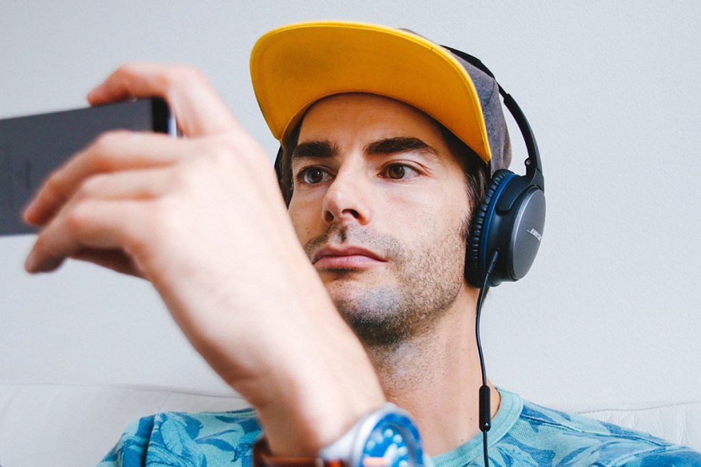 Ein Mann trägt Kopfhörer und schaut auf ein Smartphone.