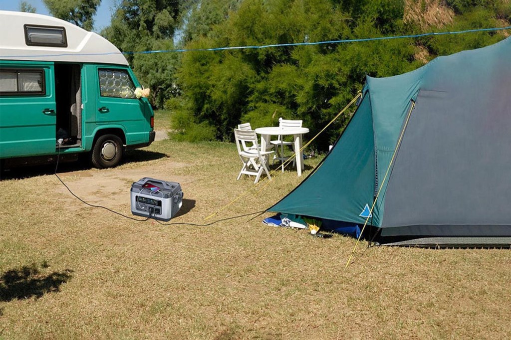 Powerstation von Revolt zwischen einem Camper und Zelt auf dem Boden.
