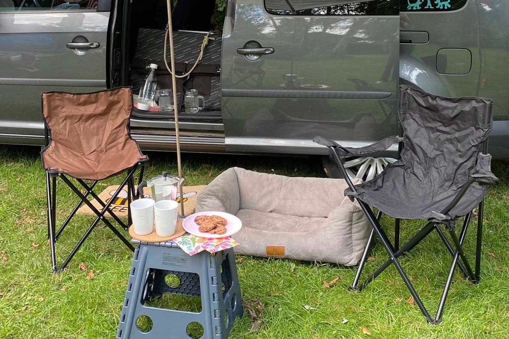 Ein Sitzplatz mit Campingstühlen, Tisch, Hundekorb und Überdachung vor einem VW Caddy.