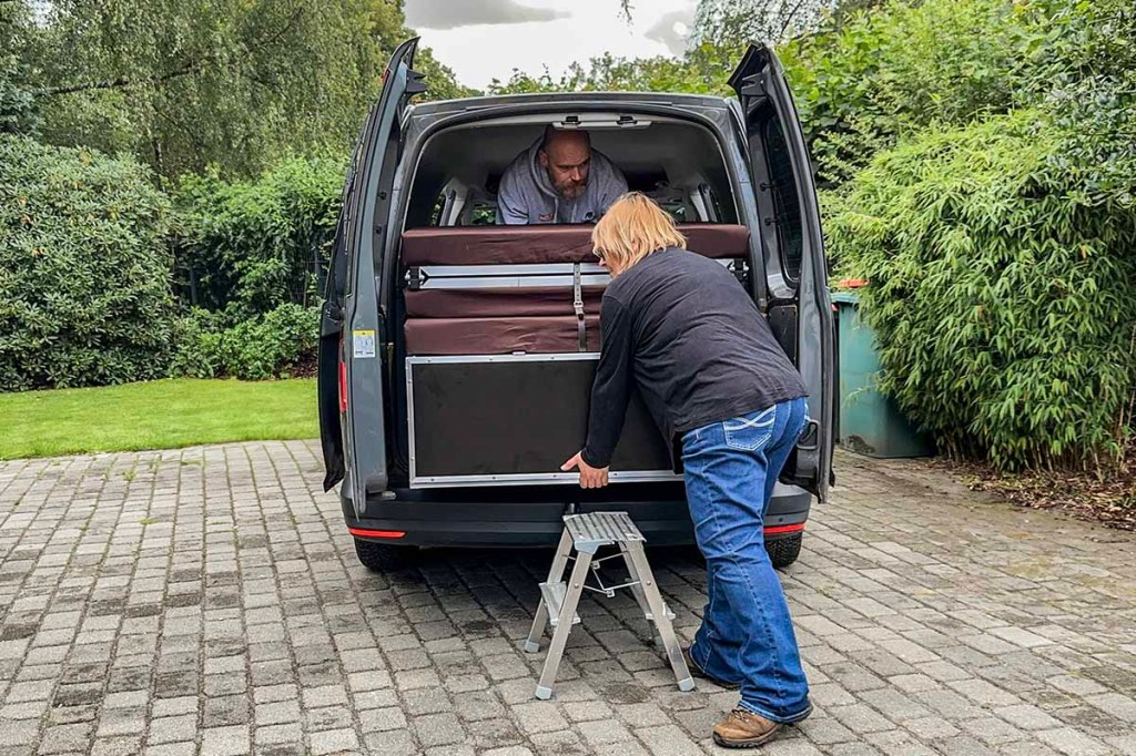 Zwei Personen bauen eine QUQUQ Camping-Box in einen VW-Caddy ein.