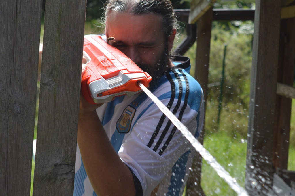 Mann mit Argentinien-Trikot, der mit einer Wasserpistole in Blickrichtung des Fotografen feuert.