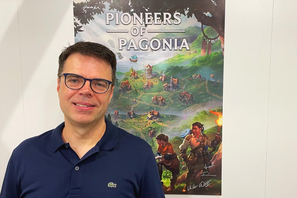 Entwickler Volker Wertich vor dem Plakat seines Spiels Pioneers of Pagonia.