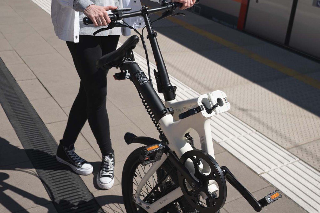 Nahaufnahme, Person mit Falt-E-Bike am Bahnsteig, Hand betätigt Bedienelement, damit das Rad elektrisch geschoben werden kann