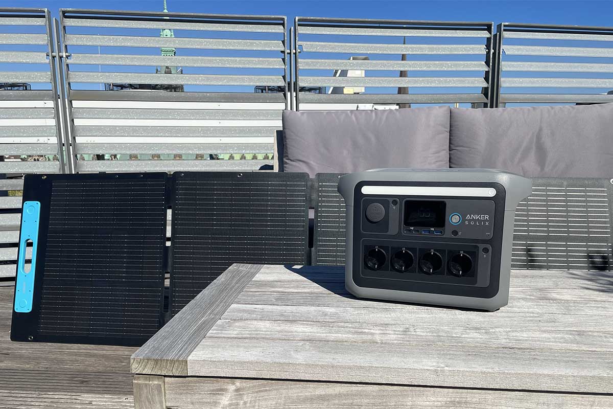 Die Anker Solix C1000 auf einem Tisch in der Sonne. Im Hintergrund steht ein Solarpanel und ein Sitzmöbel.