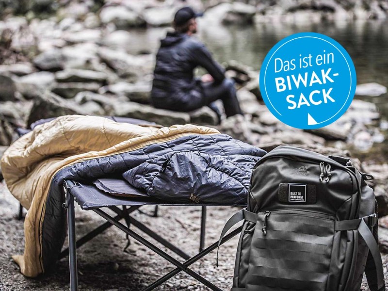 Schlafsack auf einer Liege neben einem Rucksack.