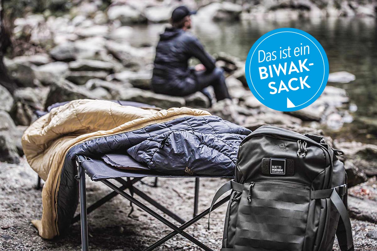 Schlafsack auf einer Liege neben einem Rucksack.